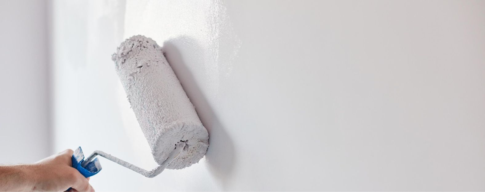 Hand hält Farbroller mit grauer Farbe an weiße Wand